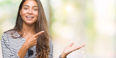 Genç güzel Arap kadın hayrete ve el ile sunulması ve parmak ile işaret ederken kameraya gülümseyen izole arka plan üzerinde güneş gözlüğü takıyor.