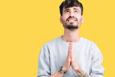 Yalvarıyor ve umut ifade yüzünde çok duygusal ve endişe ile birlikte elleriyle dua izole arka plan üzerinde kazak giyen genç yakışıklı adam. Bağışlanmak. Din kavramı.