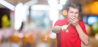 Genç yakışıklı adam giyen kırmızı t-shirt üzerine izole arka plan sizin parmak el kamerasıyla ağzına, utanç ifadesi işaret eden gülme