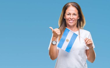 Arjantin bayrağı işaret ve başparmak kadar mutlu yüz gülümseyen tarafı ile gösteren izole arka plan üzerinde tutan orta yaş İspanyol kadın