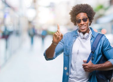 Afro Amerikalı adam giyen kulaklık ve sırt çantası üzerinde arka plan ile bir fikir ya da gülen yüz, bir numara ile parmak işaret soru sürpriz izole