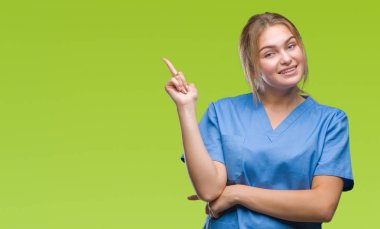 Yüzünde kocaman bir gülümseme ile izole arka plan üzerinde cerrah üniforma giyen genç beyaz hemşire kadın kameraya bakarak yan el ve parmak ile işaret.