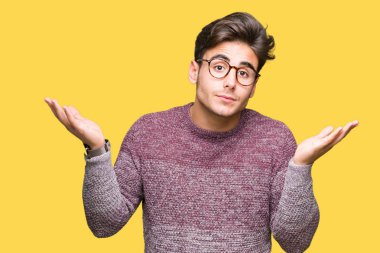 İzole arka plan clueless ve şaşkın bir ifadeyle kollar ve eller kaldırdı üzerinde gözlük takan yakışıklı delikanlı. Şüphe kavramı.