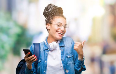 İşaret ve başparmak kadar mutlu yüz gülümseyen tarafı ile gösteren izole arka plan üzerinde akıllı telefon kullanan genç örgülü saç Afro-Amerikan öğrenci kız