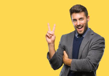 Genç yakışıklı iş adamı mutlu yüz zafer işareti yaparken kameraya göz kırpıyor ile gülümseyen izole arka plan üzerinde. İki numaralı.