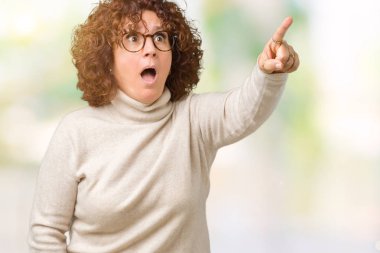 Boğazlı kazak ve gözlük izole arka plan ile sürpriz devam et, parmakla üzerinde giyen güzel orta ager üst düzey kadın ağzı açık ifade, önünde bir şey hayret