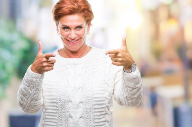 Fotoğraf makinesi ile mutlu ve komik yüz için parmakları işaret izole arka plan üzerinde kış kazak giyen Atrractive üst düzey beyaz Kızıl saçlı kadın. İyi enerji ve vibes.