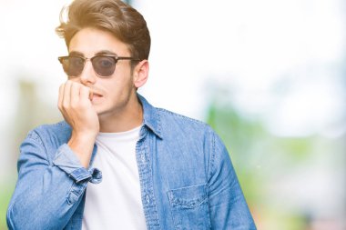 Genç yakışıklı adam stresli ve gergin ile izole arka plan üzerinde güneş gözlüğü takıyor tırnak ısırma dudaklarından eller. Anksiyete sorunu.