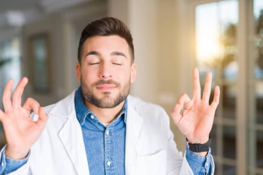 Genç yakışıklı Doktor adam klinikte rahatla ve gülümseyen gözlerle parmak ile meditasyon jest yapıyor kapalı. Yoga kavramı.