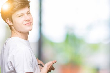 Açık el ile doğal gülümseyen girmek için davet izole arka plan üzerinde rahat beyaz t-shirt giyen genç yakışıklı adam