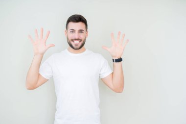 Gösterilen ve parmakları ile işaret izole arka plan üzerinde rahat beyaz t-shirt giyen genç yakışıklı adam kendinden emin ve mutlu gülümseyerek süre on numara.
