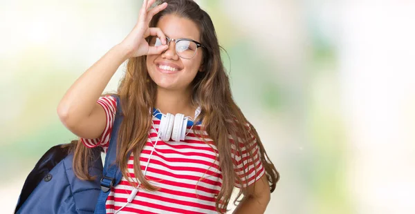年轻美丽的黑发学生妇女戴着耳机和背包在孤立的背景做确定的手势与手微笑 眼睛通过手指看着快乐的脸 — 图库照片
