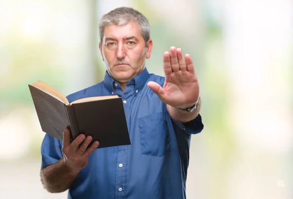 英俊的高级教师在孤立的背景下阅读一本书 张开手做停止标志 用严肃而自信的表情 防守姿态 — 图库照片