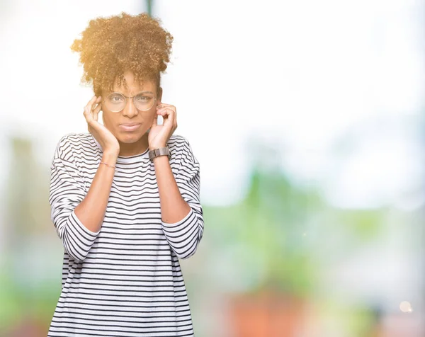 Beautiful young african american woman wearing glasses over isolated background covering ears with fingers with annoyed expression for the noise of loud music. Deaf concept.