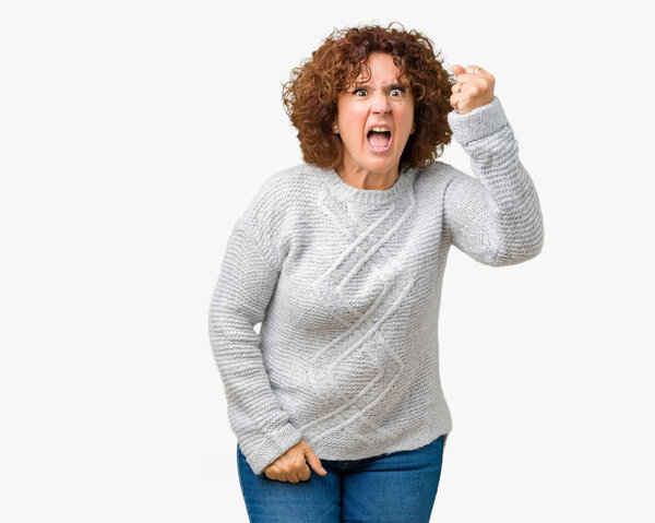 Beautiful middle ager senior woman wearing winter sweater over isolated background angry and mad raising fist frustrated and furious while shouting with anger. Rage and aggressive concept.