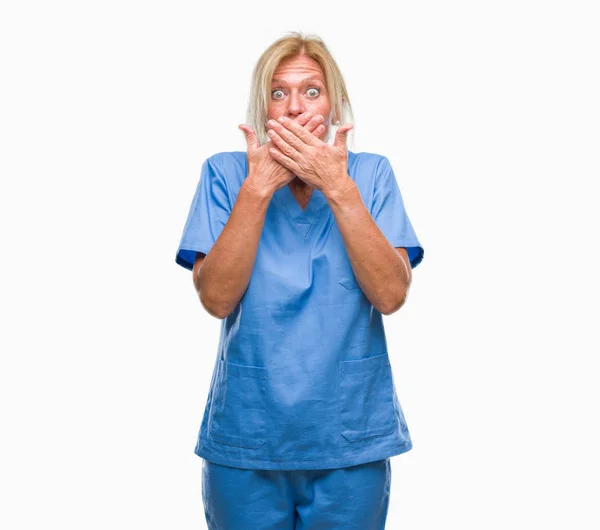 中年金发碧眼的妇女穿着医生护士制服在孤立的背景震惊覆盖嘴与手的错误 秘密概念 — 图库照片