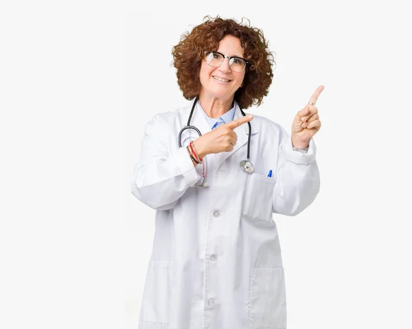 中间的高级医生妇女在孤立的背景微笑着 看着镜头指向镜头 用两只手和手指指着一边 — 图库照片