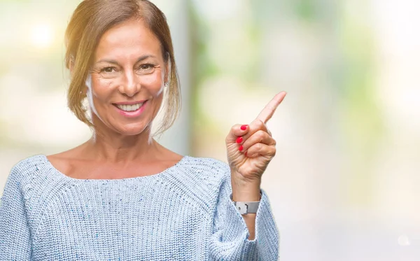 Middle age senior hispanic woman wearing winter sweater over isolated background with a big smile on face, pointing with hand and finger to the side looking at the camera.