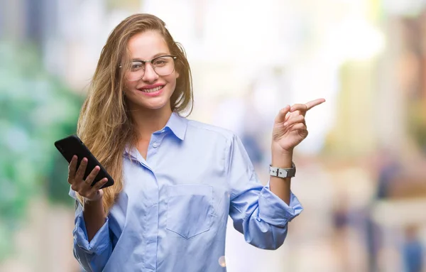 年轻美丽的金发女商人使用智能手机在孤立的背景非常高兴用手和手指指向身边 — 图库照片