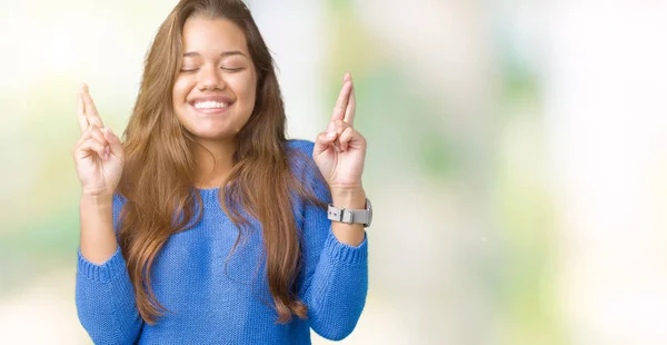 年轻美丽的黑发女人穿着蓝色毛衣在孤立的背景微笑交叉手指与希望和眼睛闭上 运气和迷信的概念 — 图库照片