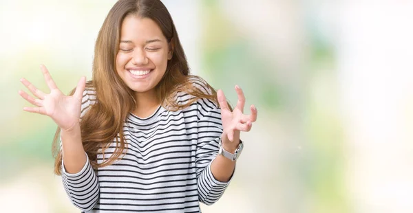 年轻美丽的黑发女人穿着条纹毛衣在孤立的背景庆祝疯狂和疯狂的成功与手臂抬起和闭上的眼睛尖叫兴奋 优胜者概念 — 图库照片