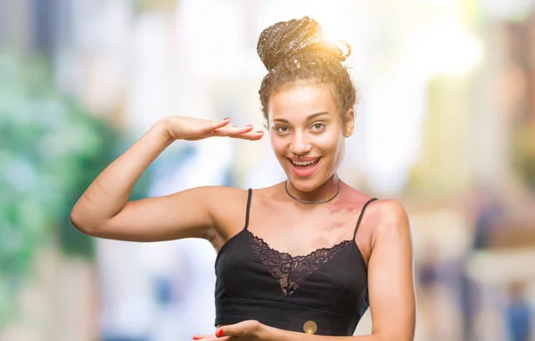 Young braided hair african american with pigmentation blemish birth mark over isolated background gesturing with hands showing big and large size sign, measure symbol. Smiling looking at the camera. Measuring concept.