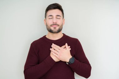 Yakışıklı delikanlı ile gülümseyen izole arka plan üzerinde bir kazak giyen kapalı gözler ve yüzünde minnettar jest ile göğüs üzerinde eller. Sağlık kavramı.