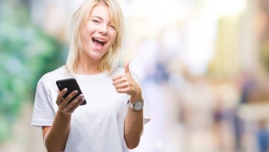 Ok işareti, başparmak ile parmak, mükemmel işareti yapıyor kocaman bir gülümseme ile izole arka plan üzerinde mutlu Smartphone kullanan genç güzel sarışın kadın