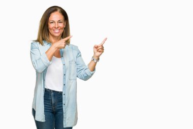 Orta yaş yetişkin kadın gülümseyerek ve iki elleri ve parmakları ile tarafına işaret kamera bakarak izole arka plan üzerinde rahat kot gömlek giymiş.