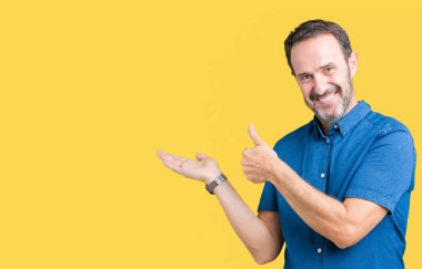 Yakışıklı orta yaş zarif komuta sizde izole arka plan gösteren palm el ve yukarıya, mutlu ve neşeli gülümseyen baş parmakları Tamam jest yapıyor