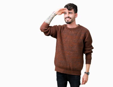 Üzerinde kış kazak giyen genç yakışıklı adam arka plan çok mutlu ve gülümseyen uzakta el ile üzerine kafa seyir izole. Arama kavramı.