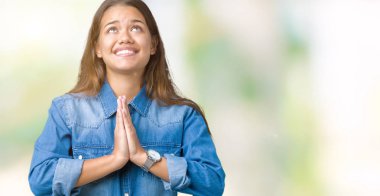 Yalvarıyor ve umut ifade yüzünde çok duygusal ve endişe ile birlikte elleriyle dua izole arka plan üzerinde mavi kot gömlek giyen genç güzel esmer kadın. Bağışlanmak. Din kavramı.