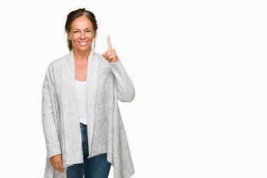 Ve kendinden emin ve mutlu gülümseyerek süre parmak numaralı yukarıyı gösteren izole arka plan üzerinde kış kazak giyen güzel orta yaş yetişkin kadın.