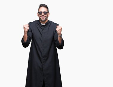 Genç Hıristiyan rahip giyen güneş gözlüğü izole arka plan ile silah kaldırdı şaşırmış ve başarı için hayran kutluyor ve açık gözler üzerinde. Kazanan kavramı.