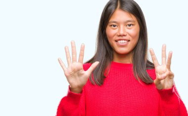 Genç Asyalı kadın giyiyor kış kazak gösterilen ve parmakları ile işaret izole arka plan üzerinde kendinden emin ve mutlu gülümseyerek süre sekiz numara.