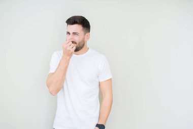 Casual beyaz t-shirt giyen bir şey pis ve iğrenç kokulu izole arka plan, dayanılmaz koku, holding nefes burun parmaklar ile yakışıklı delikanlı. Kötü kokuyor kavramı.