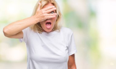 Mahcup ifadeyle parmaklarımın arasından seyir orta yaş sarışın kadın yüz ve gözler el ile kapsayan şok bakmak izole arka plan.