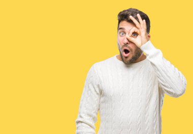 Sürpriz yüz, göz parmaklarının arasından seyir ile ok jest yapıyor izole arka plan üzerinde kış kazak giyen genç yakışıklı adam şok. İmansız ifade.