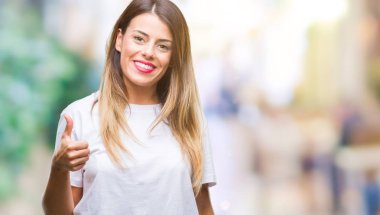 Genç güzel kadın hareketi el ile mutlu yaşasın yapıyor arka plan casual beyaz t-shirt üzerine izole. Kameraya bakarak başarı gösteren ile ifade onaylama.