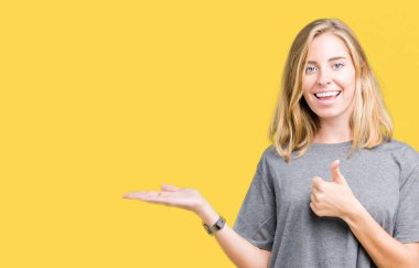 İzole arka plan gösteren palm el üzerinde büyük boy rahat t-shirt giyen ve yukarıya, mutlu ve neşeli gülümseyen baş parmakları Tamam jest yapıyor güzel genç kadın