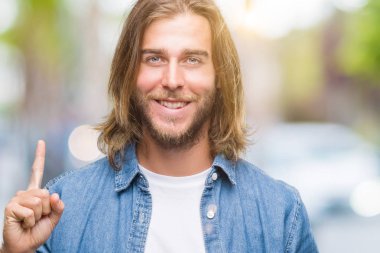 Ve kendinden emin ve mutlu gülümseyerek süre parmak numaralı yukarıyı gösteren izole arka plan üzerinde uzun saçlı yakışıklı delikanlı.