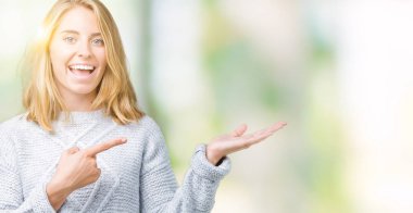 Hayret ve el ile sunulması ve parmak ile işaret ederken kameraya gülümseyen izole arka plan üzerinde kış kazak giyen güzel genç kadın.