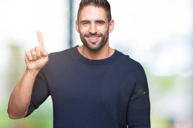 Ve kendinden emin ve mutlu gülümseyerek süre parmak numaralı yukarıyı gösteren izole arka plan üzerinde kazak giyen genç yakışıklı adam.