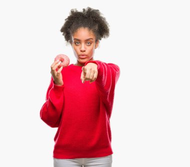 Genç afro Amerikalı kadın üzerinde çörek yeme kamera ve size parmak ile işaret arka plan izole, el işareti, pozitif ve kendinden emin bir jest ön