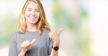 Güzel genç kadın üzerinde büyük boy rahat t-shirt giyen izole arka plan emin gülümseyen arkasından el ve kadar başparmak ile işaret