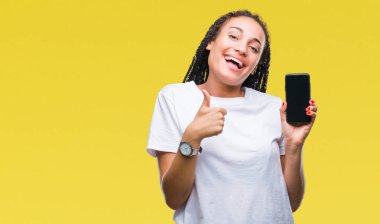 Genç izole arka plan üzerinde ekran akıllı telefon ok işareti, başparmak ile parmak, mükemmel işareti yapıyor kocaman bir gülümseme ile mutlu gösteren Afro-Amerikan kız saç örgülü