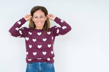 Üzerinde kalp kazak giyen güzel orta yaş kadın arka plan gülen çekerek kulakları parmaklar, komik jest ile izole. Seçmelere sorun