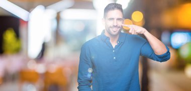 İzole genç yakışıklı adam arka plan işaretçi el parmak yüz ve burun, neşeli gülümseyen