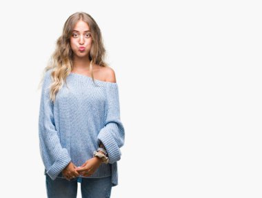 Komik surat ile yanakları şişirme izole arka plan üzerinde kış kazak giyen güzel genç sarışın kadın. Ağız ile hava, deli ifade şişirilmiş.