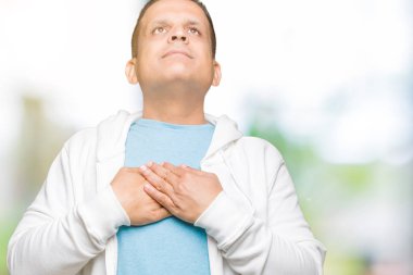 Orta yaş Arap adam ile gülümseyen izole arka plan üzerinde sweatshirt giyen kapalı gözler ve yüzünde minnettar jest ile göğüs üzerinde eller. Sağlık kavramı.